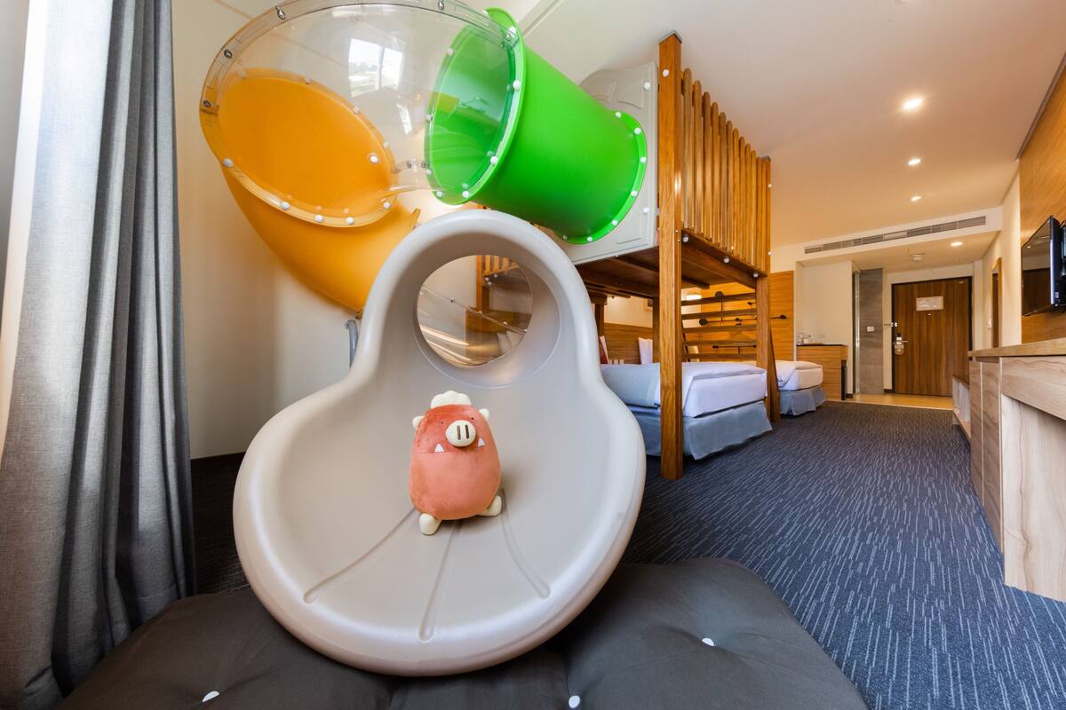 A hotel room with a bunk bed, a slide, and a small pig plush toy.