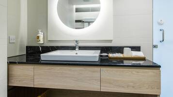 Un baño moderno con un lavamanos blanco, encimera negra, mueble de tocador de madera y una balanza en el estante inferior.