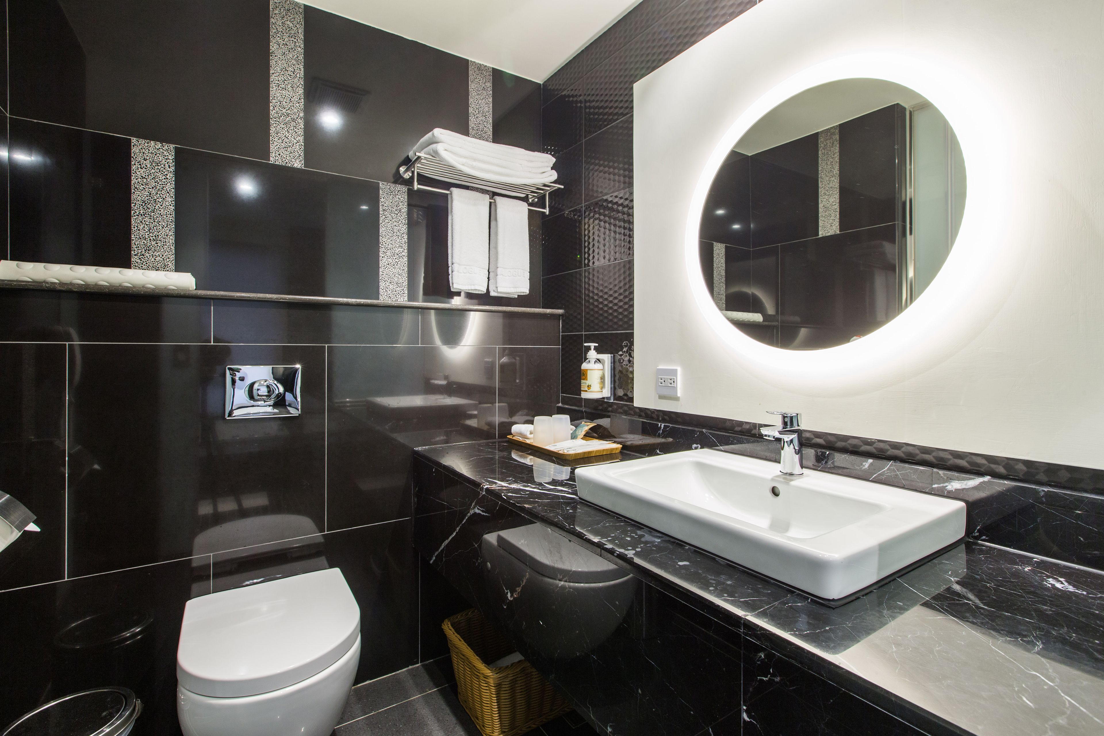 A modern bathroom with a white sink, black marble countertops, a round mirror, and a toilet.