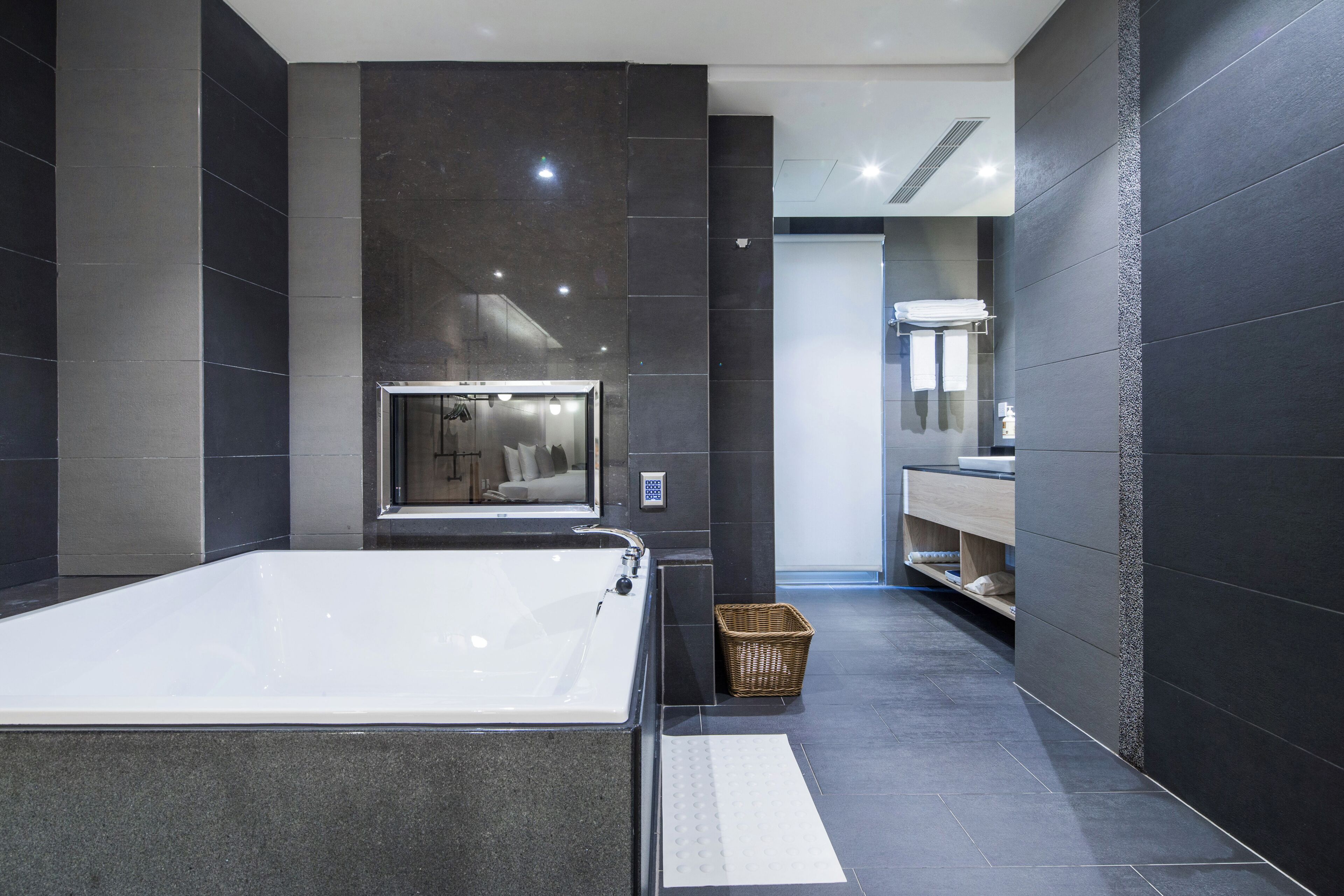 A modern bathroom with a large bathtub, dark tiled walls, and a visible shower area.