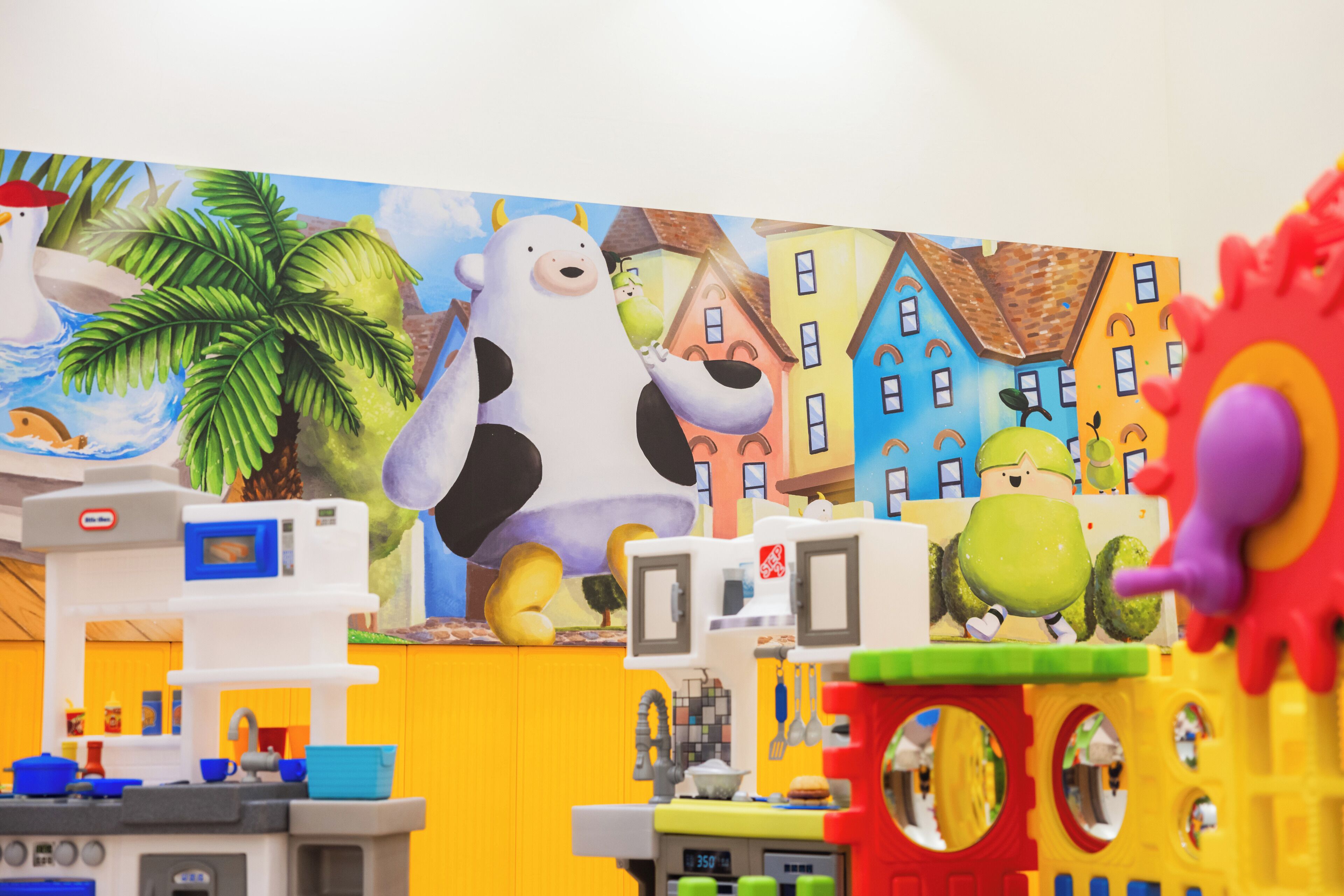 A colorful play area with a mural, a large cow figure, and various toys.