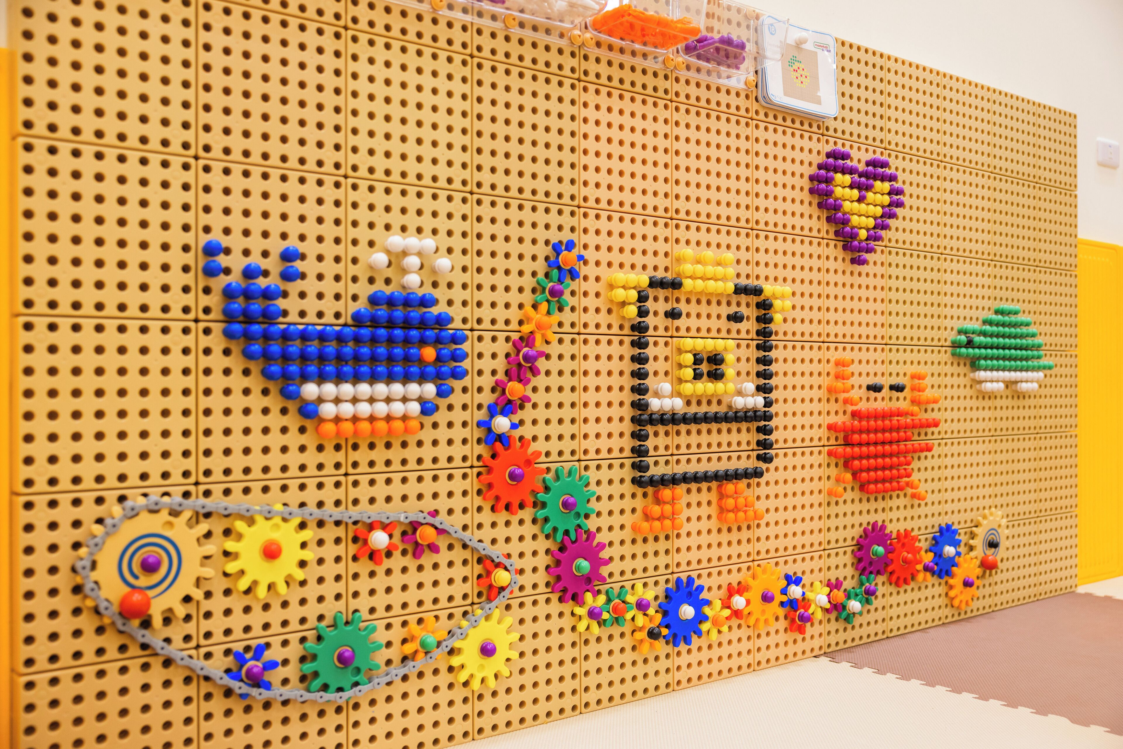A pegboard with various colorful objects and structures, including gears, flowers, and a heart shape.