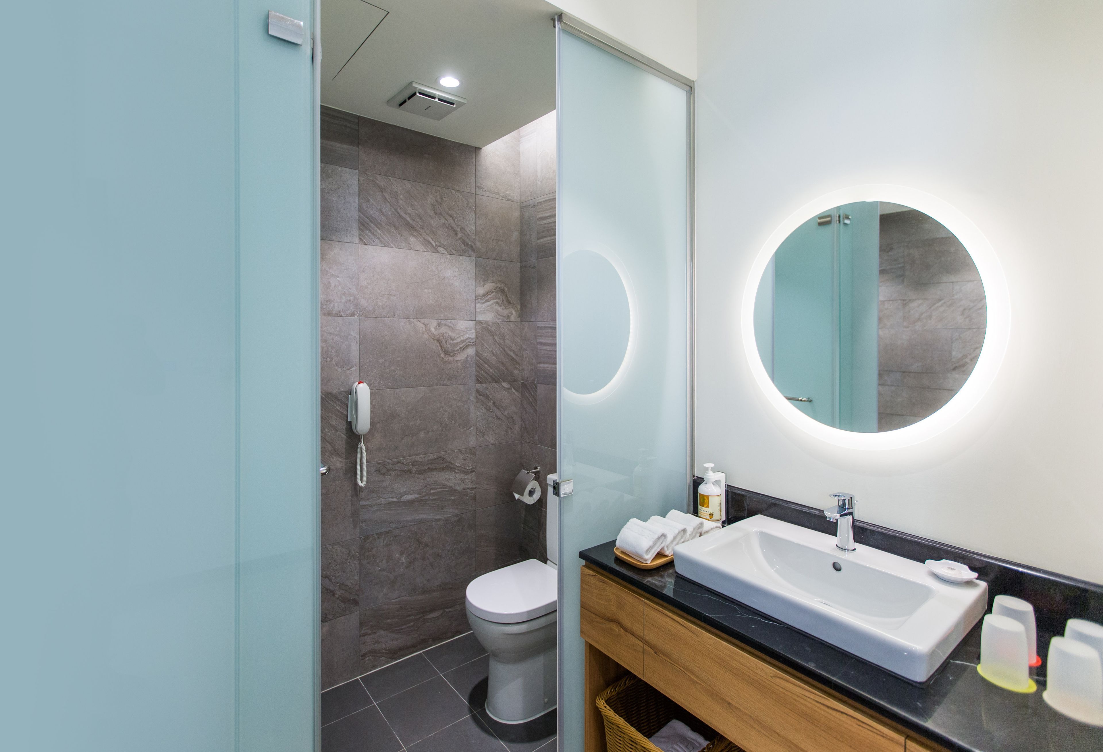 A modern bathroom with a glass shower enclosure, a toilet, a sink with a mirror, and a wooden vanity.