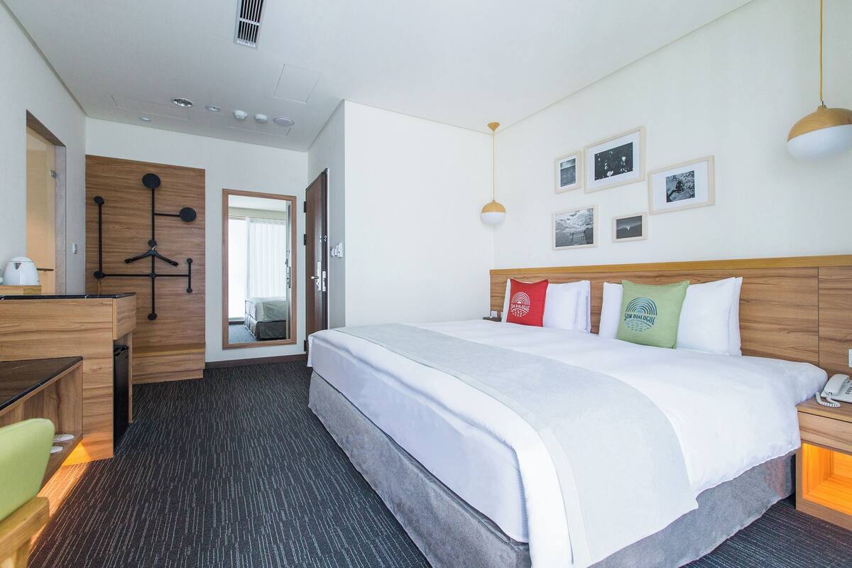 A hotel room with a large bed, a desk, a chair, and a wardrobe.