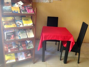 Ein kleiner Leseplatz mit einem roten Tisch und schwarzen Stühlen, umgeben von Bücherregalen voller verschiedener Bücher.