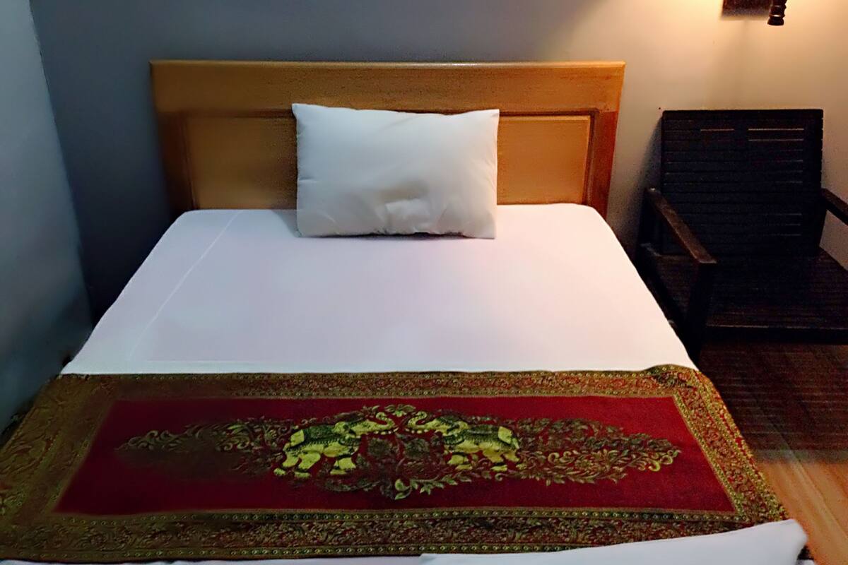 A neatly made bed with a white pillow and a red and gold patterned bedspread.