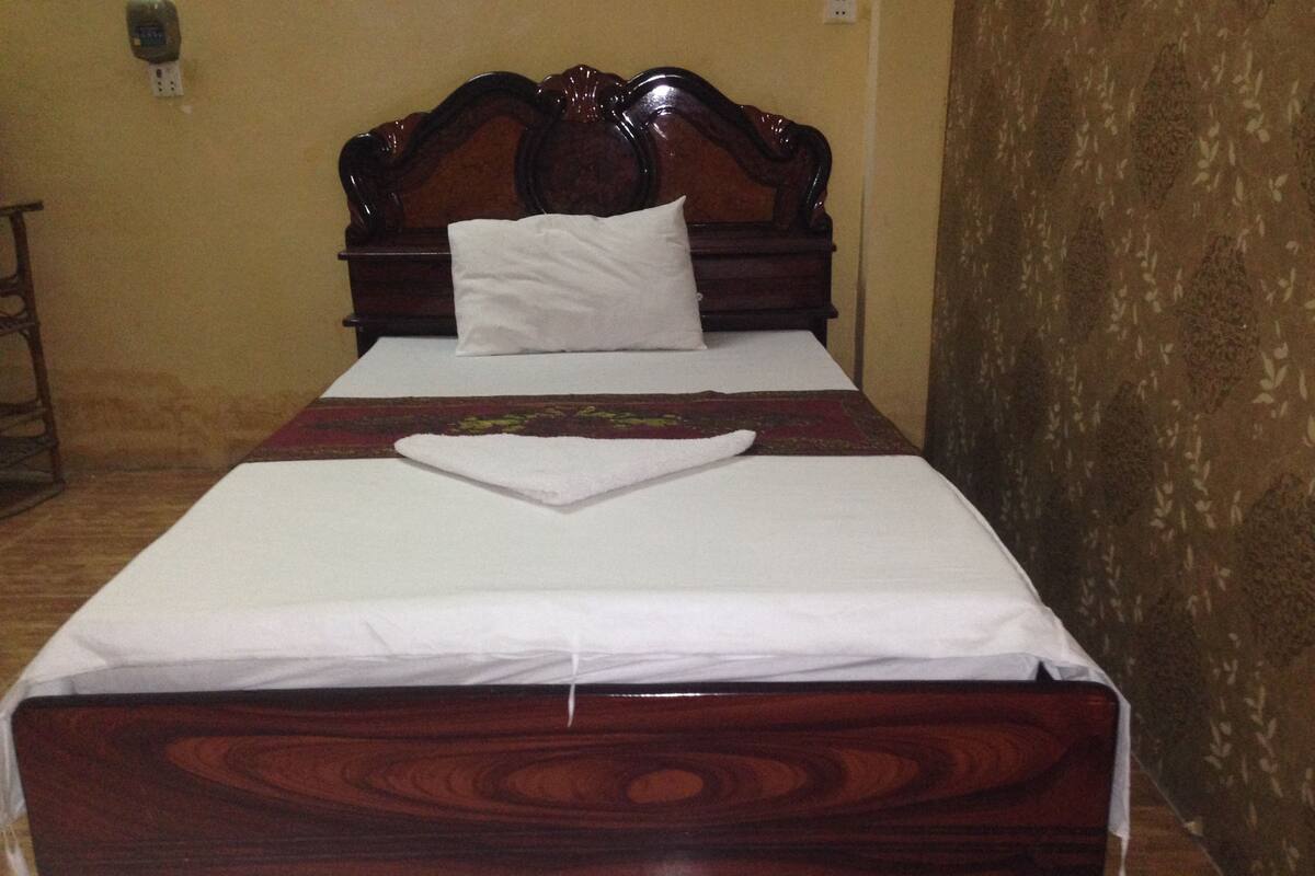 A neatly made bed with a wooden headboard, white bedding, and a decorative red and green bedspread.