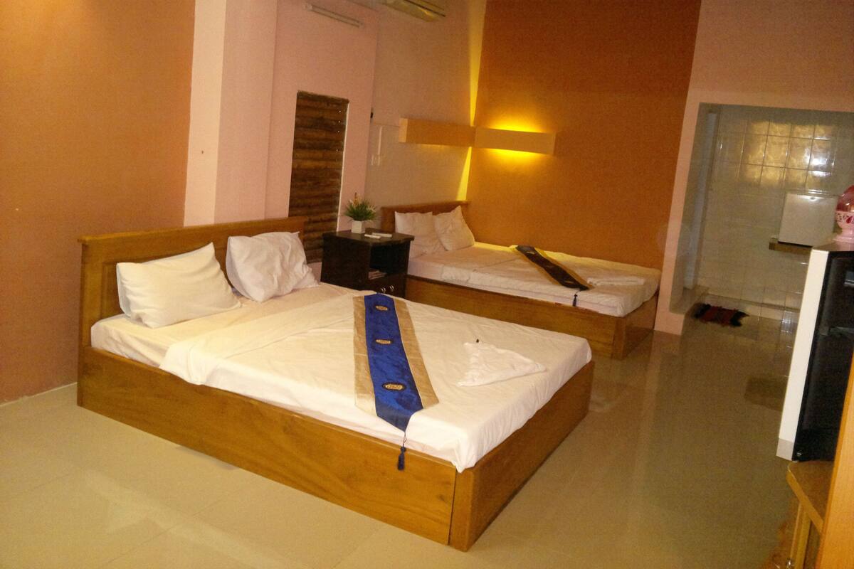 A hotel room with two beds, a nightstand, a lamp, and a small table.