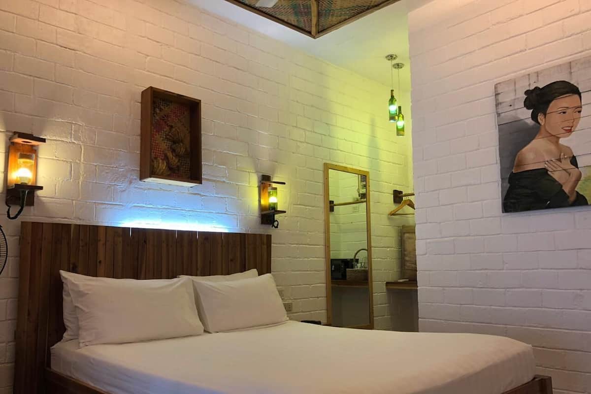A neatly made bed with white linens in a room with white brick walls and wooden headboard.