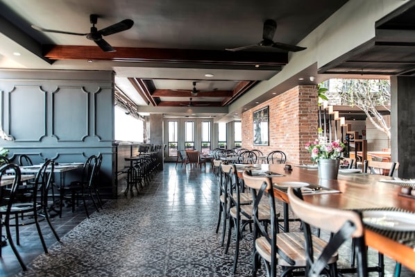 A spacious restaurant with high ceilings, exposed brick walls, and a mix of wooden and metal furniture. - Aquarius Hotel & Urban Resort Phnom Penh (Phnom Penh)
