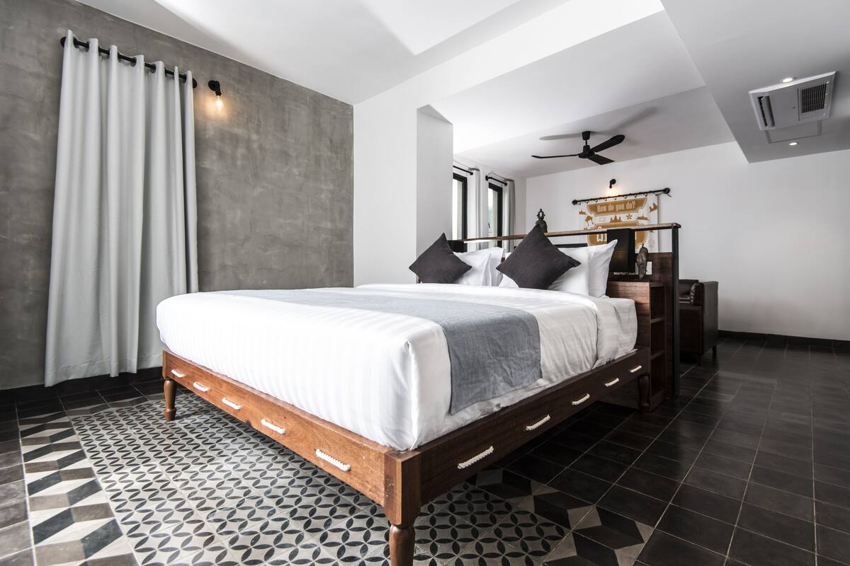 A modern bedroom with a large bed, a nightstand, a ceiling fan, and a wall-mounted air conditioner.