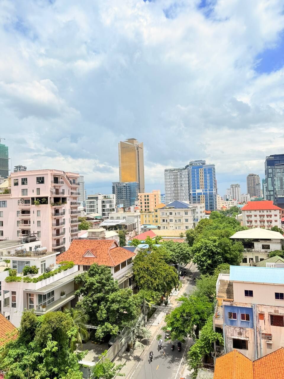 Un paysage urbain avec des immeubles à plusieurs étages, dont un gratte-ciel imposant, entouré de verdure et sous un ciel dégagé.