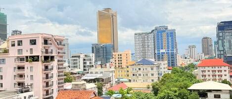 Un paysage urbain avec des immeubles à plusieurs étages, dont un gratte-ciel imposant, entouré de verdure et sous un ciel dégagé.