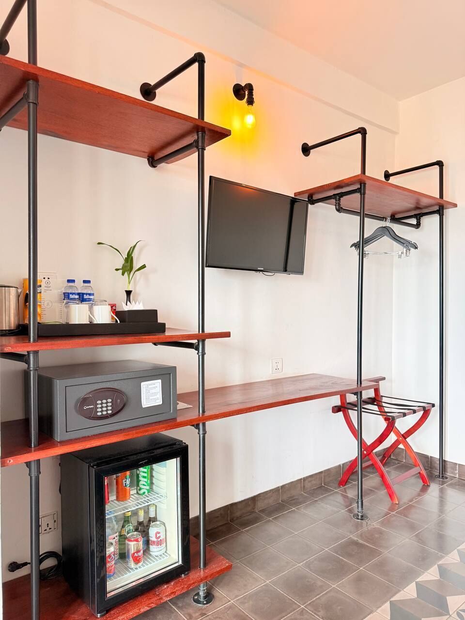 A compact hotel room with a TV mounted on the wall, a minibar, a small refrigerator, and a red folding chair.