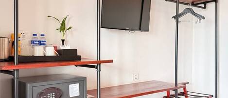 A compact hotel room with a TV mounted on the wall, a minibar, a small refrigerator, and a red folding chair.