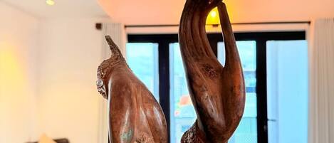 A sculpture of a dog and a hand on a stand in a room with a ceiling fan and a window.