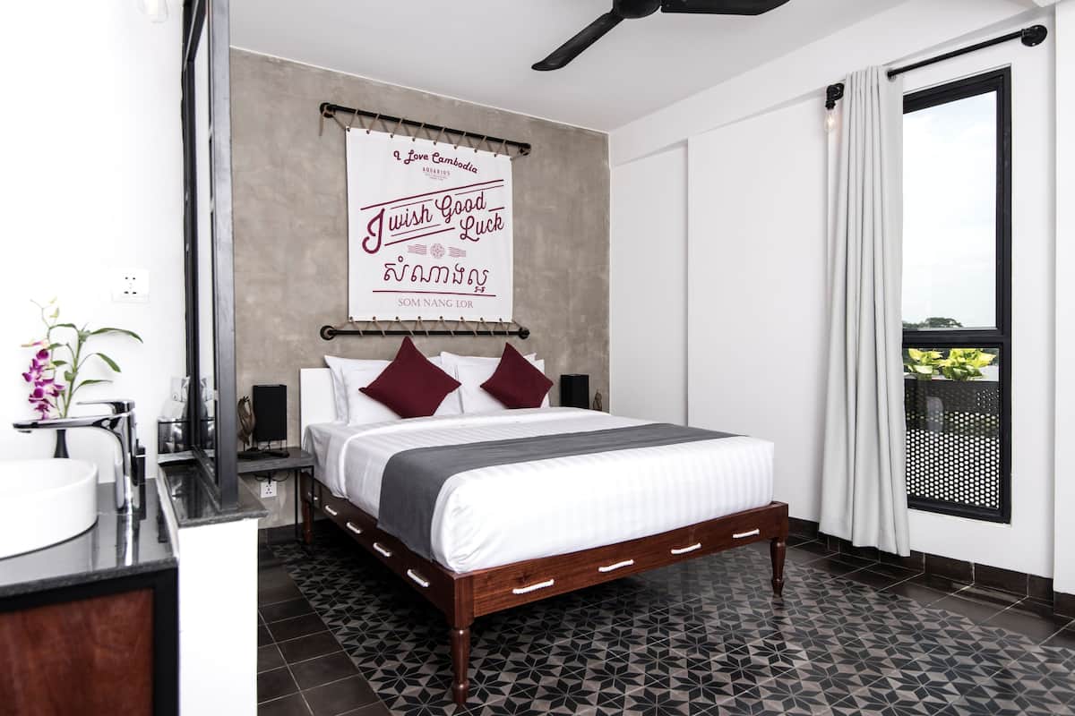 A modern hotel room with a large bed, a bathroom with a sink and mirror, and a window with curtains.