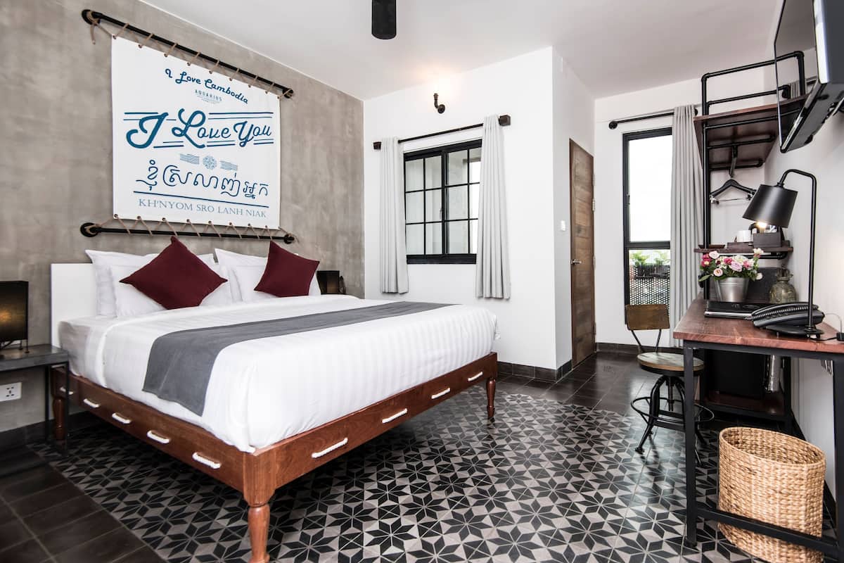 A bedroom with a bed, a desk, a chair, a hanging sign, and a window.