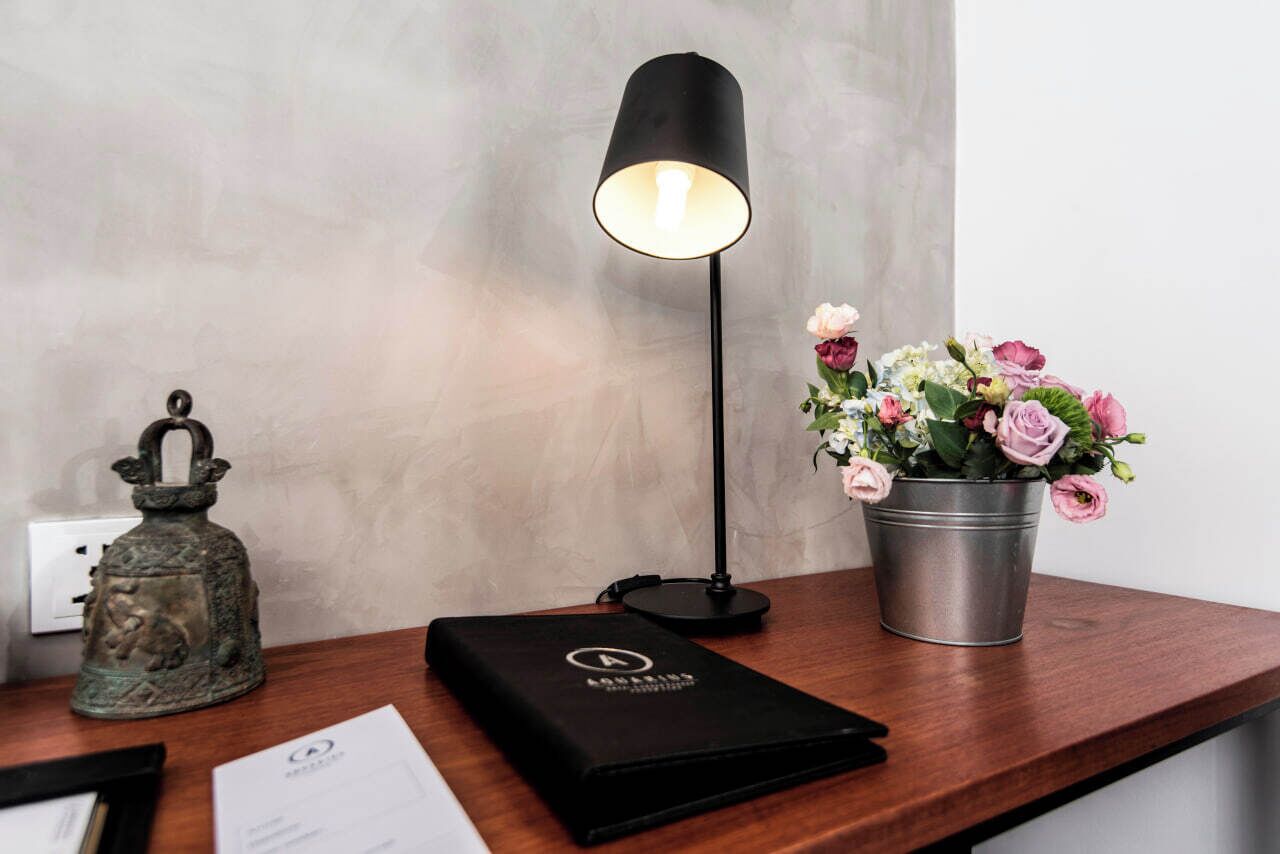 A desk with a black desk lamp, a metal bell, a black folder, and a metal bucket with flowers.