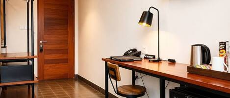 A hotel room with a desk, chair, television, and a refrigerator.
