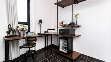 Espaço de trabalho compacto com escrivaninha, cadeira e um frigorífico pequeno.