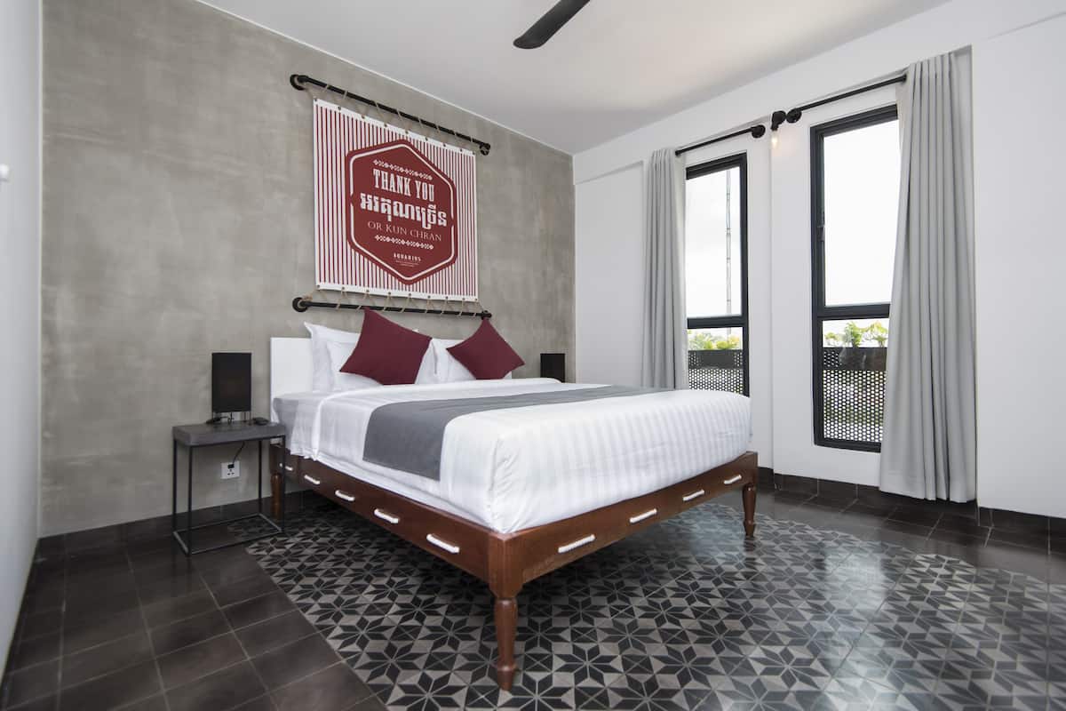 A modern hotel room with a large bed, a nightstand, a wall-mounted sign, and a view through a window.