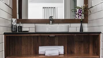 A modern bathroom with a wooden vanity, a large mirror, and a black tiled floor.