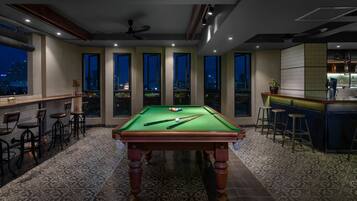 A pool table in a room with large windows, a bar area, and bar stools.