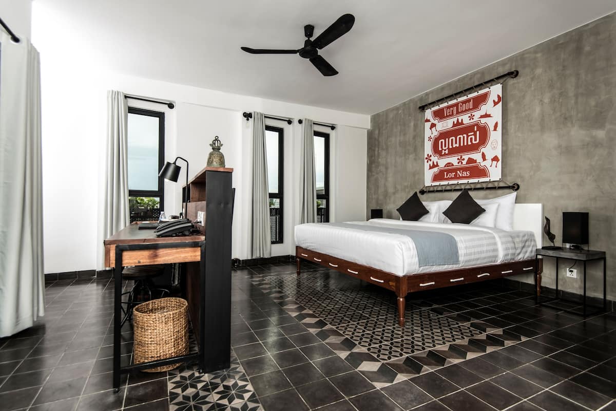A modern bedroom with a bed, desk, and chair, a ceiling fan, and a large window with curtains.