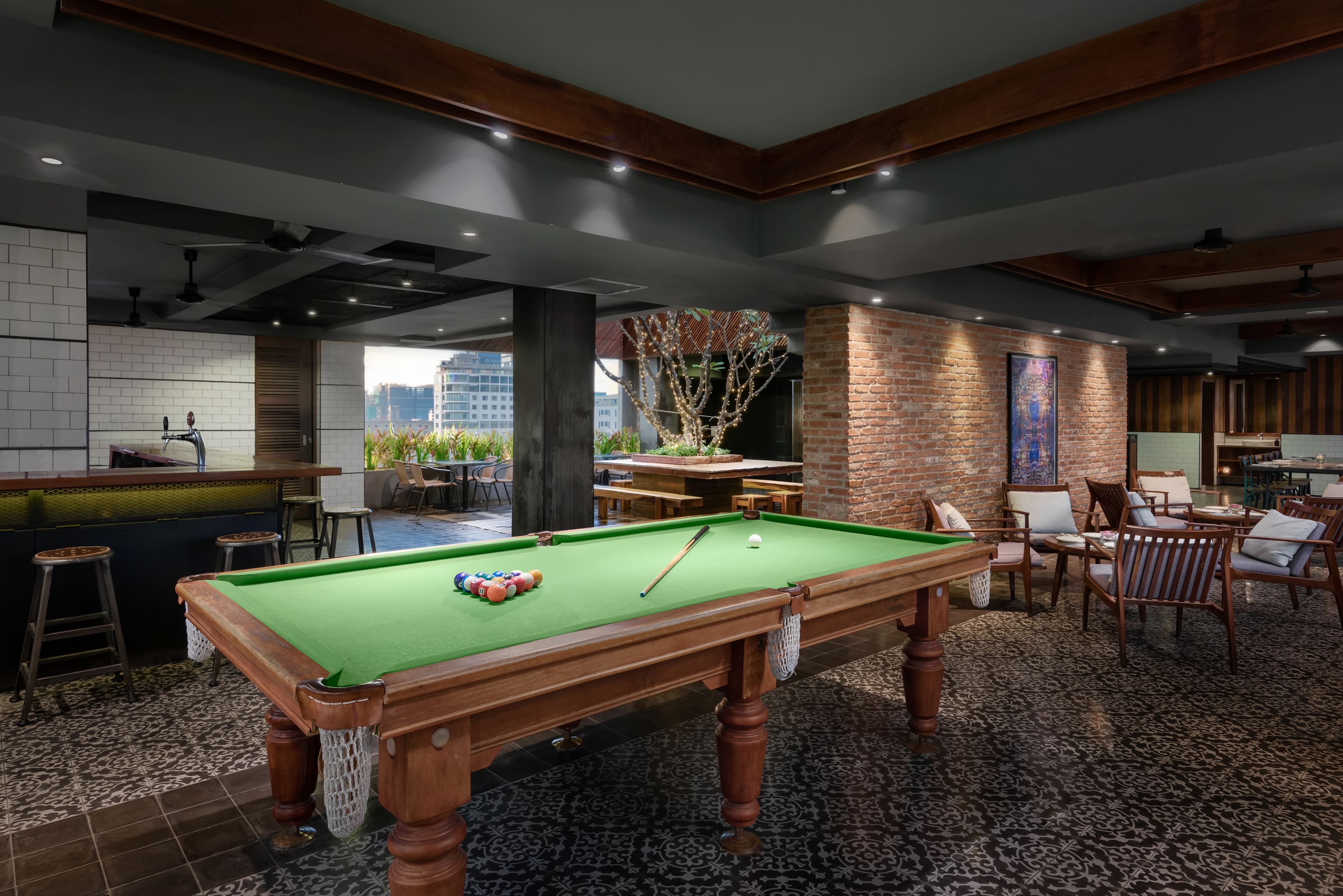 A pool table in a room with a bar, seating area, and a view of buildings.