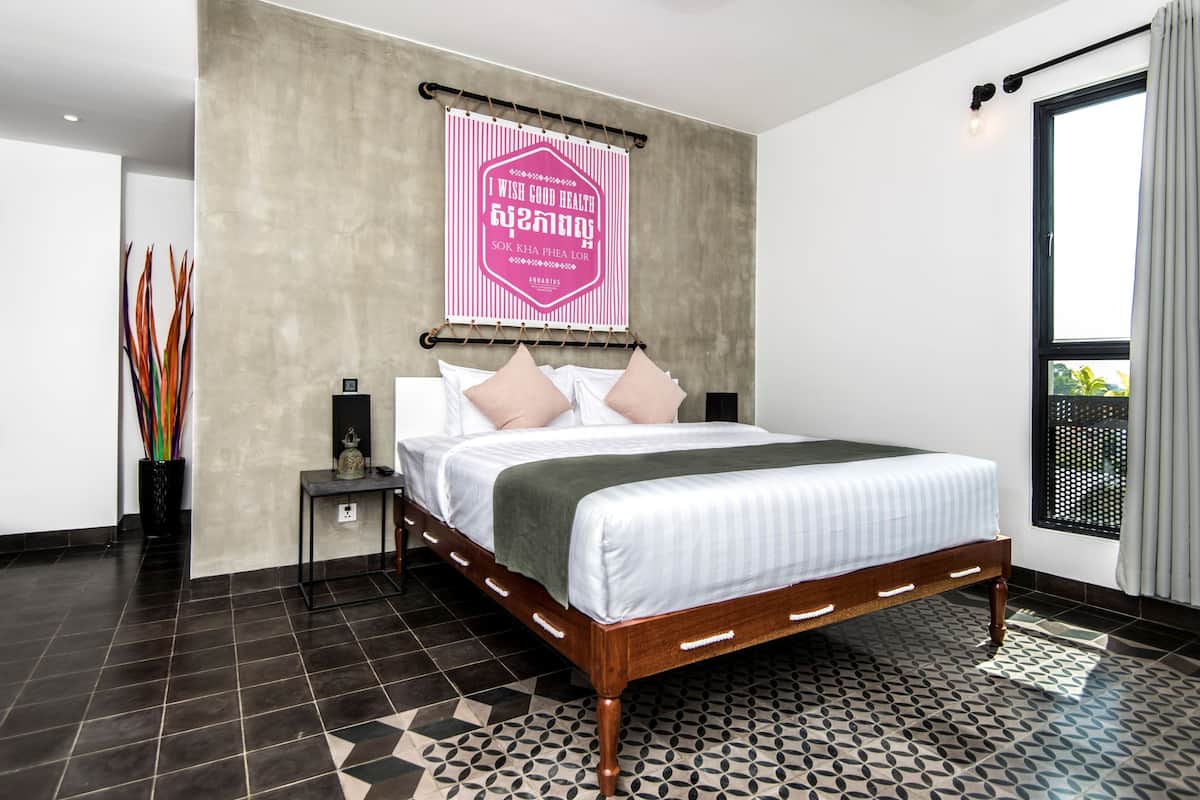 A modern bedroom with a large bed, a nightstand, a wall-mounted light, and a window with curtains.