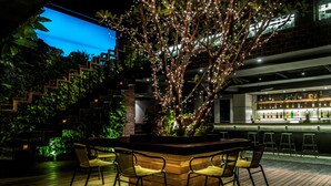 An outdoor bar area with a wooden table and chairs, surrounded by greenery and illuminated by string lights. - Aquarius Hotel & Urban Resort Phnom Penh (Phnom Penh)