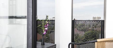 A balcony with a black perforated partition, a wicker chair, and a small table with a vase of purple flowers.