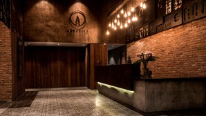A reception area with a wooden reception desk, a brick wall, and a patterned carpet. - Aquarius Hotel & Urban Resort Phnom Penh (Phnom Penh)