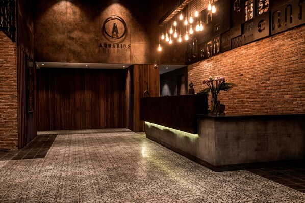 A reception area with a wooden reception desk, a brick wall, and a patterned carpet. - Aquarius Hotel & Urban Resort Phnom Penh (Phnom Penh)