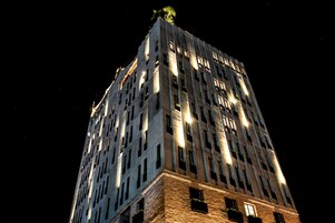 Un edificio alto e iluminado con un diseño arquitectónico moderno, que cuenta con varios pisos y una estructura destacada en la azotea.