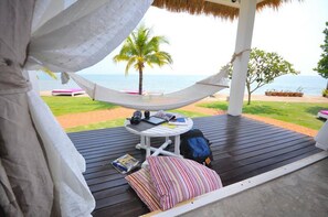 A hammock on a wooden deck overlooking a beach with palm trees and lounge chairs. - Sea Coco Resort (Tha Mai)