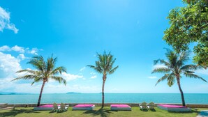 Un salón junto a la playa con cuatro sillones reclinables y una piscina pequeña, con vistas al océano.