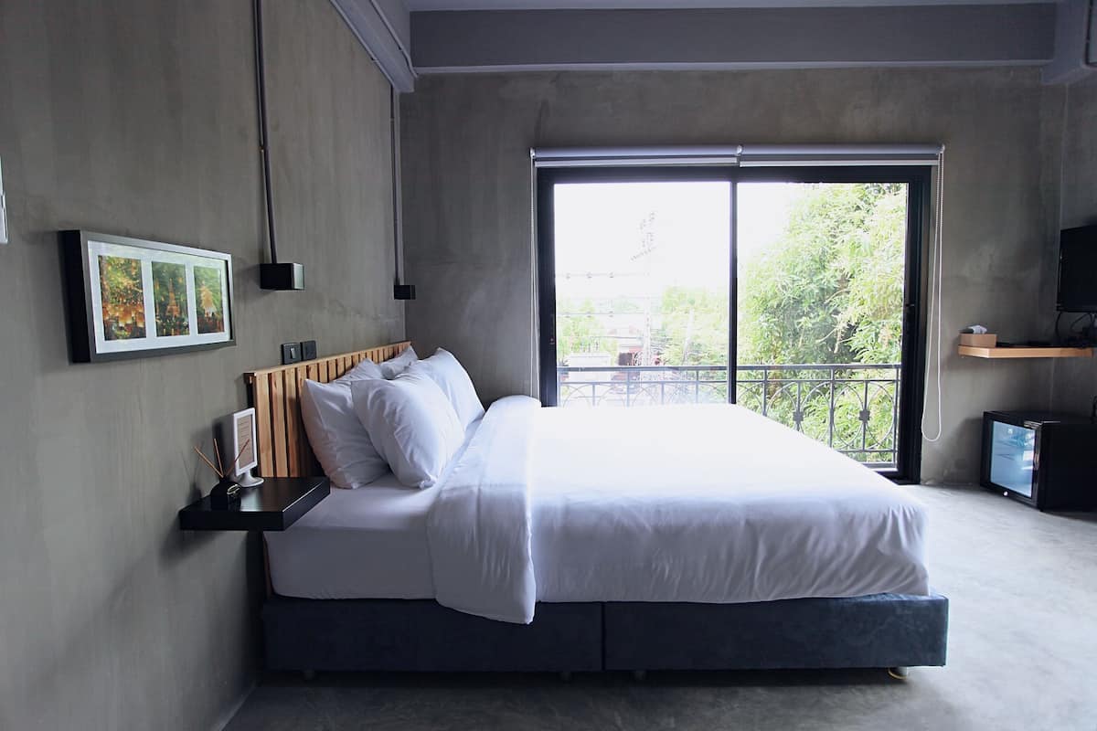 A modern bedroom with a large bed, a bedside table with a lamp, a picture frame, and a TV on a stand.