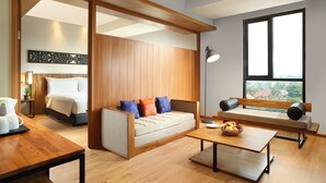 A modern hotel room with a wooden ceiling, a sofa with cushions, a bed, a dining table, and a large window offering a view.