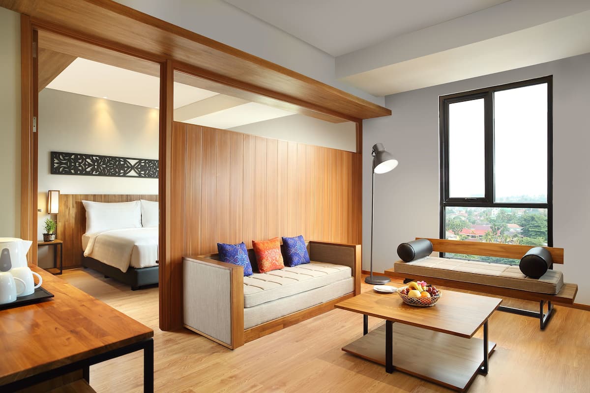 Une chambre d’hôtel moderne avec un plafond en bois, un canapé avec des coussins, un lit, une table à manger et une grande fenêtre donnant sur un paysage.