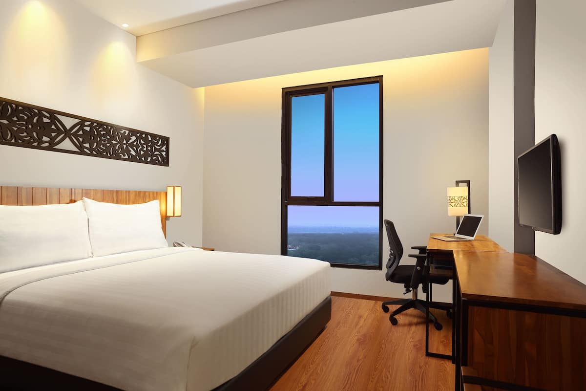Une chambre d’hôtel avec un grand lit, un bureau avec un ordinateur portable, une télévision et une fenêtre donnant sur le paysage.