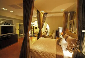 A hotel room with a large bed, a television, and a seating area with a sofa and armchairs.
