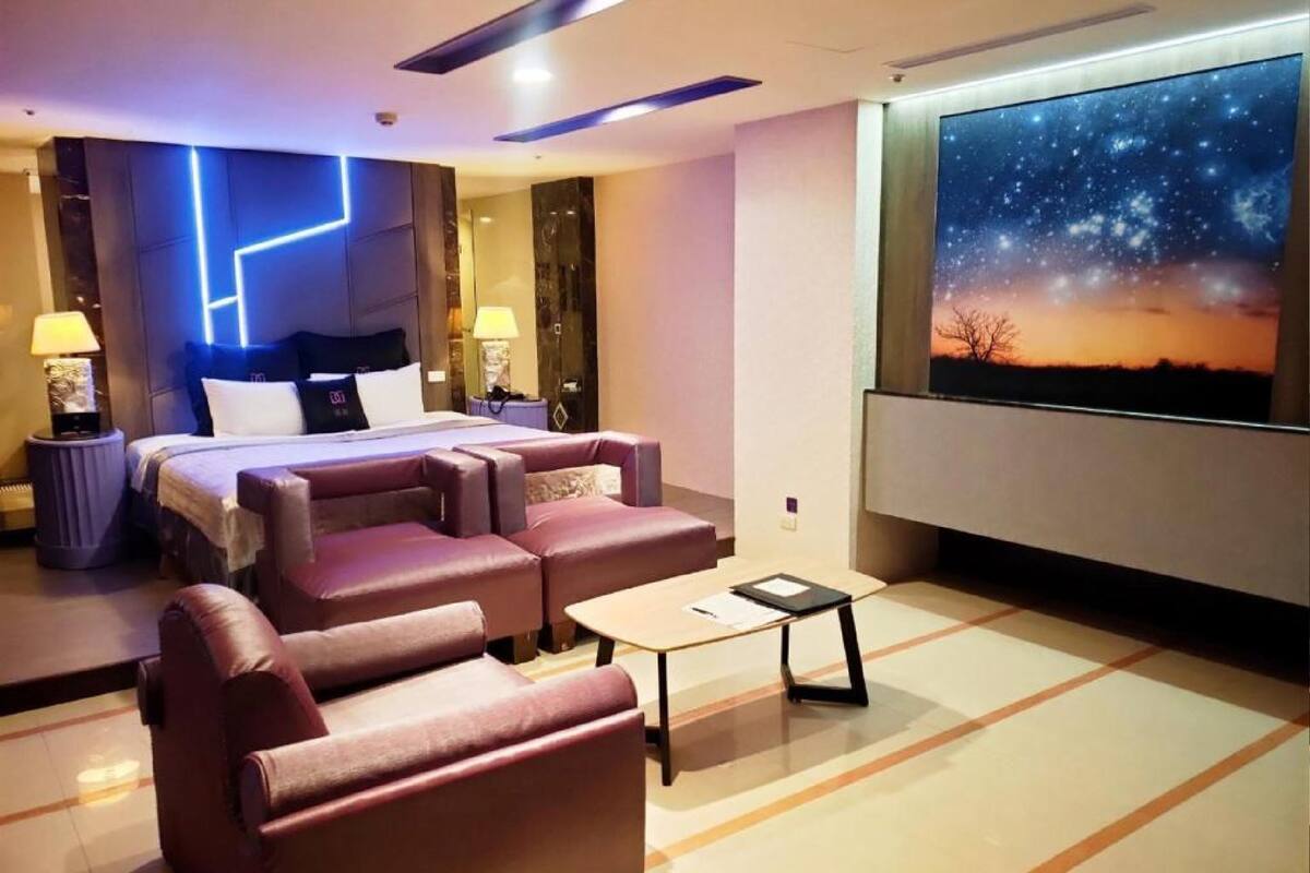 A modern hotel room with a bed, a sofa, a small table, and a large wall mural of a starry night sky.