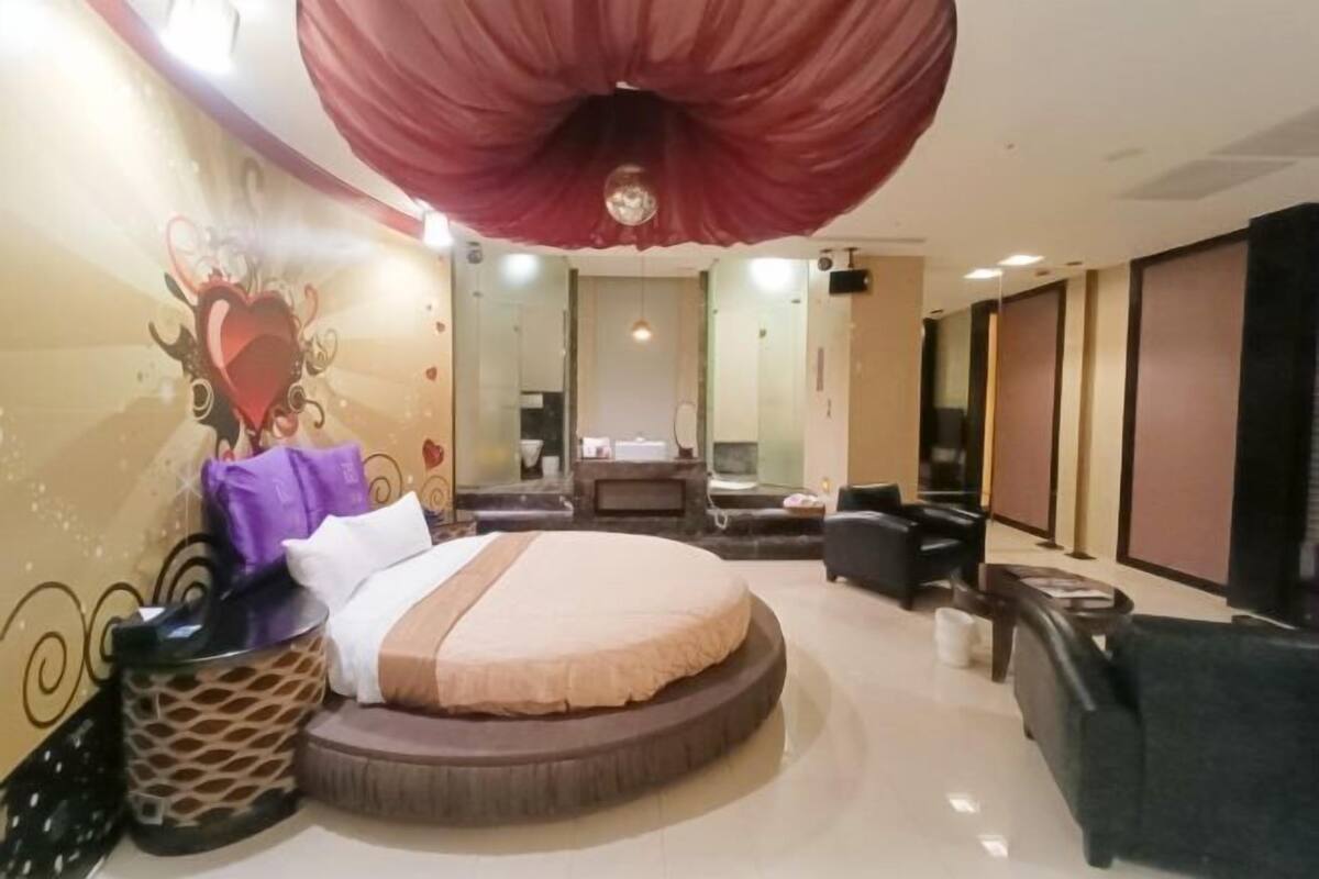 A hotel room with a round bed, a TV, a sofa, and a large mirror.