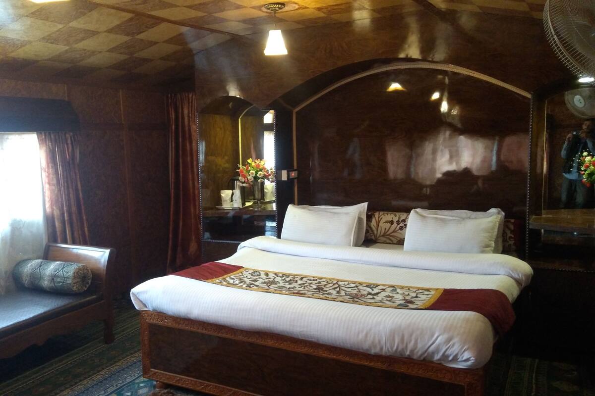 Um quarto de madeira com uma cama grande, um banco e um espelho.
