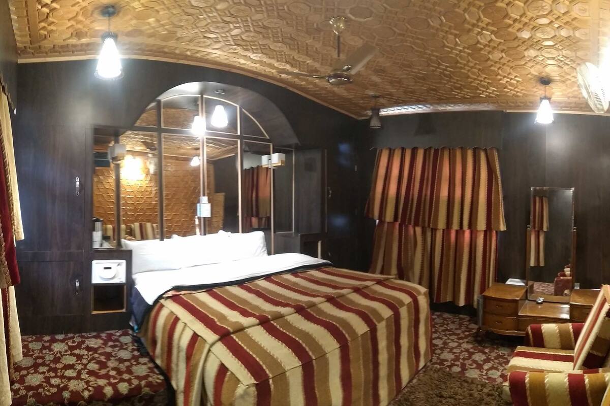 Quarto de hotel com uma cama grande, uma escrivaninha, uma cadeira, um espelho e uma janela com cortinas.