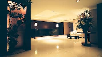 A modern lobby with a reception desk, seating area, and decorative plants.