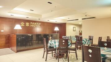 A family hotel reception area with wooden paneling, a reception desk, and several tables with chairs.