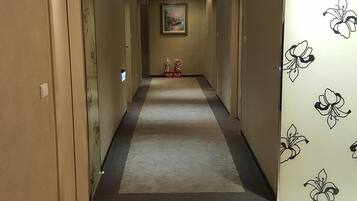 A hotel hallway with a carpeted floor, a painting on the wall, and a floral wallpaper on one side.